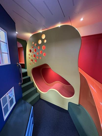 Clourful indoor children’s playground with green stairs, bleu floor and wall, and red slide